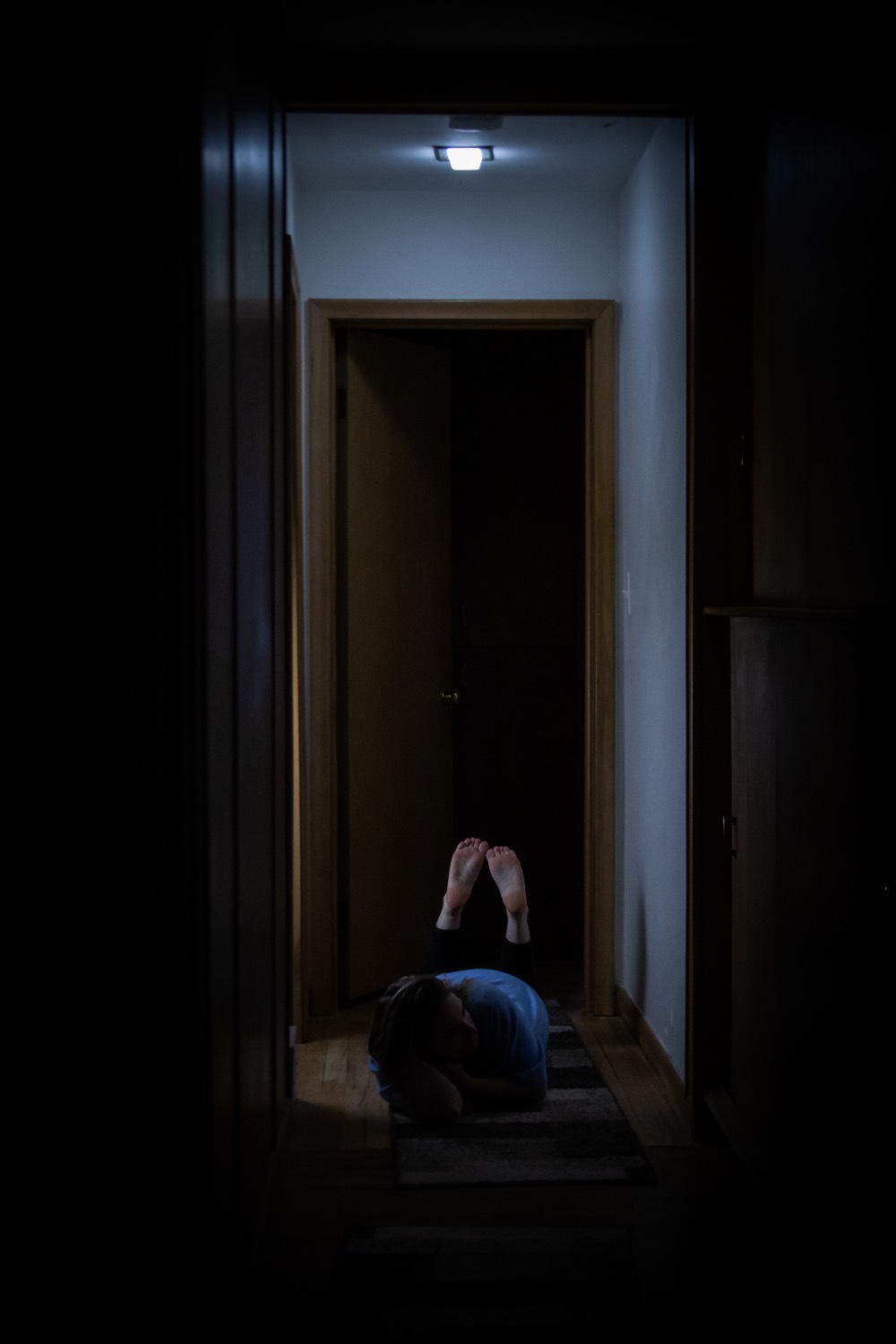 Very dark image of a dimly lit hallway with someone lying down on their stomach